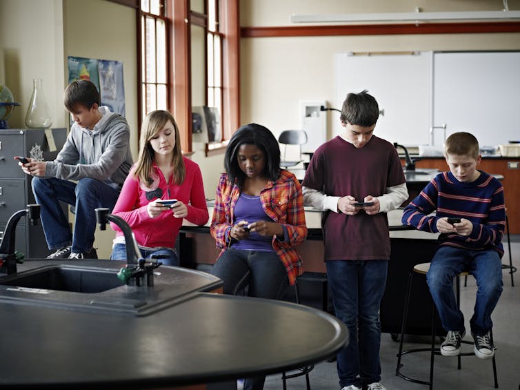 A group of students stare down at their phones in a classroom.