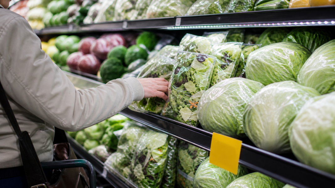 Shopper considering bagged salad and iceberg lettuce in a grocery produce aisle